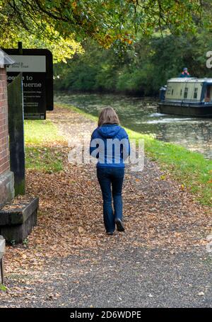 Junge Frau, die am Flussufer entlang auf einem Kanalpfad mit einem schmalen Boot im Hintergrund läuft. Stockfoto