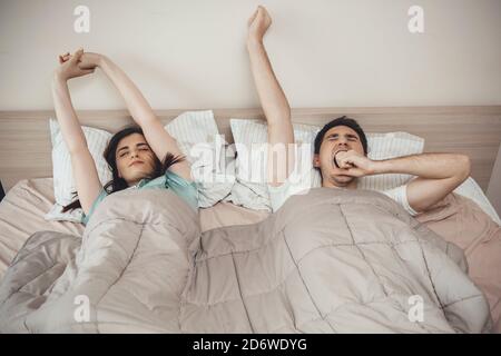 Kaukasisches Paar gähnend im Bett und Stretching am Morgen Bedeckt mit einer Steppdecke Stockfoto