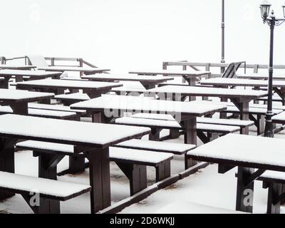 Holz identische Tische mit Bänken mit Schnee bedeckt stehen in Eine Reihe auf der Terrasse eines Straßencafés Stockfoto