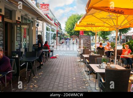 Kunden, darunter ein kleiner Hund, genießen ein Straßencafé im touristischen Zentrum von Warnemunde, Deutschland Stockfoto