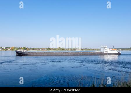 Ein kommerzielles Trockenfrachtschiff segelt im Sommer oder Frühherbst entlang des Flusses. Horizontale Ausrichtung, selektiver Fokus. Stockfoto