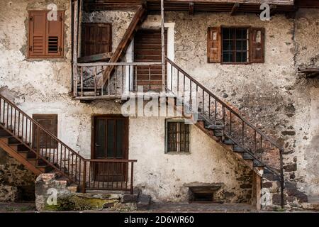 Ein altes Haus im italienischen Dorf Mezzano, im Trentino Südtirol mit weißen Wänden und braunen Holzfenstern, Türen und Geländer Stockfoto