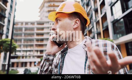 Porträt eines jungen Handwerkers, der beim Stehen auf der Baustelle anruft. Techniker, der auf einer Baustelle telefoniert. Builder in Helm Stockfoto
