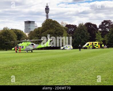 Ein krankes Kind wird aus der Kinderluftambulanz entfernt und in einen Krankenwagen im Regent's Park im Zentrum von London verladen. Der Patient wird zum nahe gelegenen Great Ormond Street Hospital gebracht. Der Hubschrauber wird von Wohltätigkeitsorganisationen finanziert und wird verwendet, um Kinder zu bewegen, die zu krank sind, um auf der Straße zu reisen. Ein Polizist räumte das Feld von Menschen, bevor der Hubschrauber landete. Die drei Transportformen sind Millionen Pfund wert und der Service ist für den Patienten nach den NHS-Regeln kostenlos. Der BT Tower ist im Hintergrund. Stockfoto