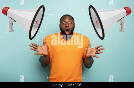 Erstaunt und schockiert Ausdruck eines Jungen, der eine erhalten Nachricht mit Lautsprechern auf cyanfarbenem Hintergrund Stockfoto