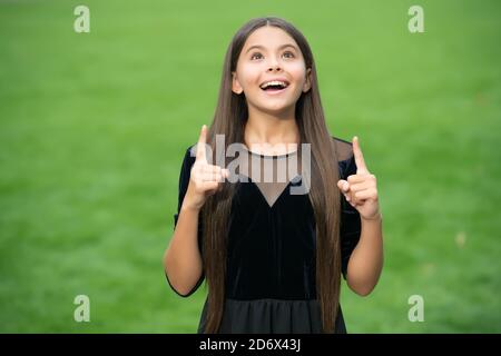 Inspiriert glücklich Mädchen mit langen Haaren in Mode Kleid Look up halten indeex Finger angehoben grünen Gras Sommer im Freien, Inspiration. Stockfoto