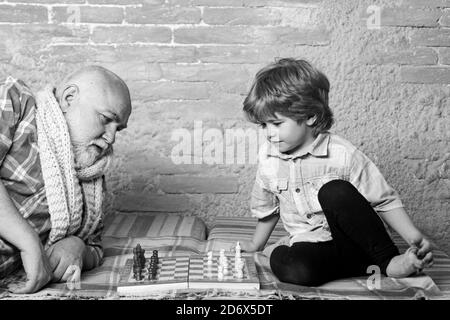 Kleiner Junge spielt Schach mit seinem Großvater. Schachfigur. Älterer Mann, der über seinen nächsten Zug in einem Schachspiel nachdenkt. Stockfoto