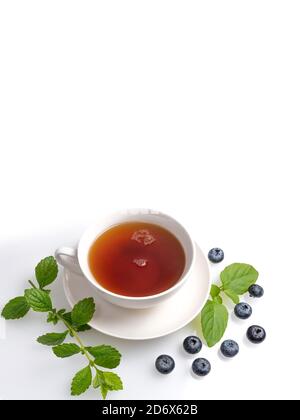 Eine Tasse schwarzen Tee auf einer Untertasse mit Minzblättern und Heidelbeeren auf einem weißen isolierten Hintergrund. Speicherplatz kopieren Stockfoto