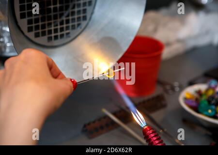 Der Künstler erhitzt das Glas mit einem Gasbrenner. Der Prozess der Herstellung von Glasschmuck. Die Hände des Meisters aus der Nähe Stockfoto