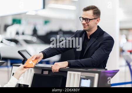 Business Reise. Hübscher junger Geschäftsmann in Anzug Holding seinen Pass und im Gespräch mit Frau am Check-in-Schalter im Flughafen Stockfoto