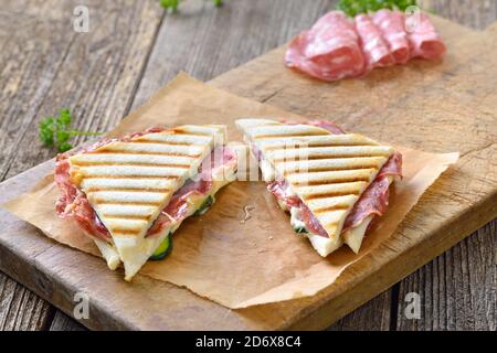 Gepresste und geröstete Doppelpanini mit italienischer Salami und Käse Serviert auf Sandwichpapier auf einem Holztisch Stockfoto
