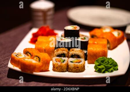 Serviert appetitliches Sushi auf weißem Teller im Café. Nahaufnahme von leckeren Sushi-Brötchen mit Wasabi und Ingwer im traditionellen japanischen Restaurant. Stockfoto