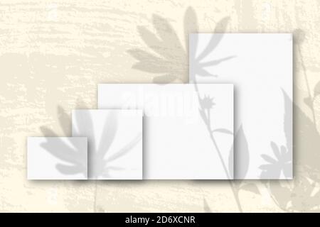Mehrere horizontale und vertikale Blätter aus weißem strukturiertem Papier vor einem gelben Wandhintergrund. Mockup mit einer Überlagerung von Pflanzenschatten. Natürlich Stockfoto