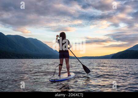 Woman Paddleboarding auf Scenic Lake bei Sonnenuntergang Stockfoto