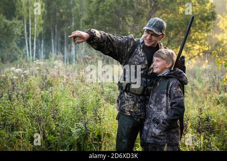 Ein kleiner Junge auf der Jagd mit einem erfahrenen Lehrer im Wald. Herbst. Jagd auf Hochland Wildvögel. Stockfoto