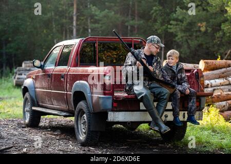 Vater in einer Mütze und sein Sohn sitzen im Auto nach der Jagd. Stockfoto