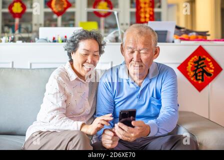 Asiatisches Seniorenpaar lächelt und schaut auf das Handy während des chinesischen Neujahrs. chinesischer Text: Frühling Stockfoto