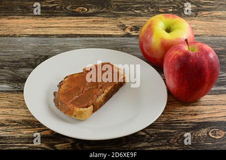 Apfelbutter auf Brotscheibe auf Weißbrotteller Und Äpfel auf dem Tisch Stockfoto