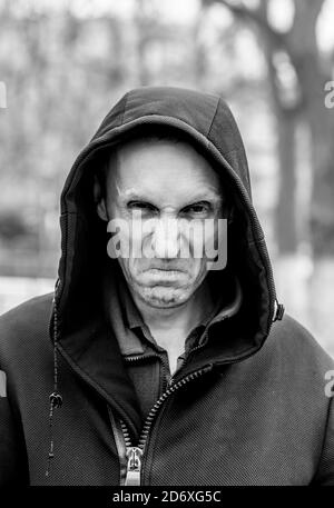 Porträt eines wütenden und unangenehmen erwachsenen kaukasischen Mannes auf einer Straße. Der Mensch sieht unangenehm aus und wirkt verrückt. Schwarz-Weiß-Aufnahme. Konzept des Ekel. Stockfoto