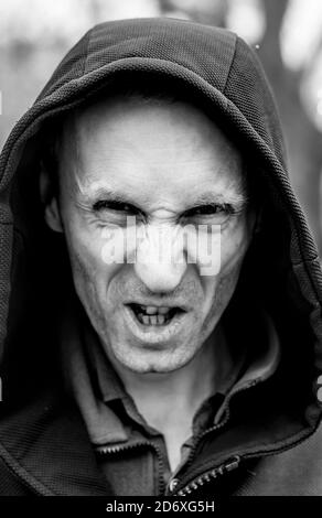 Porträt eines wütenden und unangenehmen erwachsenen kaukasischen Mannes auf einer Straße. Der Mensch sieht unangenehm aus und wirkt verrückt. Schwarz-Weiß-Aufnahme. Konzept des Ekel. Stockfoto