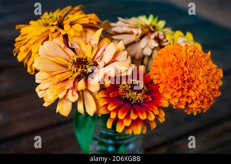 Verschiedene Schnittblumen in einem Glas-Einmachglas auf einem dunklen Holztisch im Freien angeordnet. Stockfoto