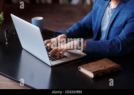 Geschäftsmann mit Laptop-Computer zu Hause. Nahaufnahme der männlichen Hände, die im Büro auf der Laptop-Tastatur tippen. Geschäft, von zu Hause aus arbeiten, online studieren Stockfoto