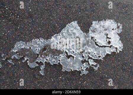 Schmelzendes Eis liegt auf einer asphaltierten Straße, abstraktes Hintergrundbild Stockfoto