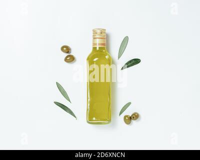 Olivenöl Glasflasche Nachbau. Draufsicht auf klare Glasflasche mit Olivenöl auf weißem Hintergrund mit grünen Oliven und frischen grünen Olivenbaumblättern. Speicherplatz kopieren. Stockfoto