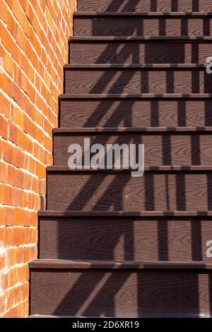 Vollrahmen abstrakte Textur Hintergrund einer braunen Holztreppe mit Metallgeländer entlang einer Außenseite vintage Lehm Ziegelwand, in direktem Sonnenlicht Stockfoto