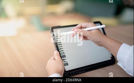 Die weibliche Hand mit digitalem Tablet mit Bleistift Touch blanken Bildschirm auf Schreibtisch Arbeitstisch am Co-Working-Raum für das neue normale Konzept. Stockfoto