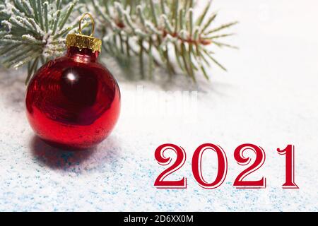 Schöne Neujahrskarte mit der Aufschrift der Nummern 2021, einer roten Kugel und einem schneebedeckten Fichtenzweig im Schnee. Stockfoto