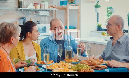 Erweiterte Familie interagierend, während eine Mahlzeit am Esstisch in der Küche. Mehrere Generationen, vier Personen, zwei glückliche Paare reden und essen während eines Gourmet-Dinner, genießen Zeit zu Hause. Stockfoto