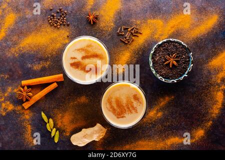 Masala Chai Tee auf schwarzem Hintergrund. Zwei transparente Gläser Masala-Tee und verschiedene Gewürze verstreut. Draufsicht Stockfoto
