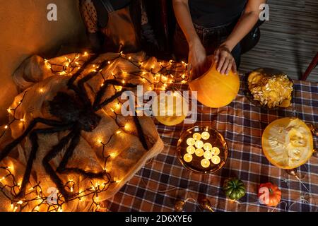 Halloween Kürbisse und große Spinne mit elektrischer Beleuchtung auf dem Tisch. Mutter und Tochter schnitzen Kürbis. Stockfoto