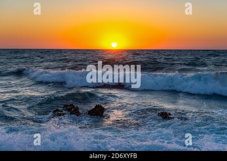 Sonnenuntergang und Sturm auf dem Meer. Große Wellen gegen die untergehende Sonne. Sommersturm auf dem Schwarzen Meer. Schönes Meeresspray mit Schaumbrüchen an der felsigen Küste. Be Stockfoto
