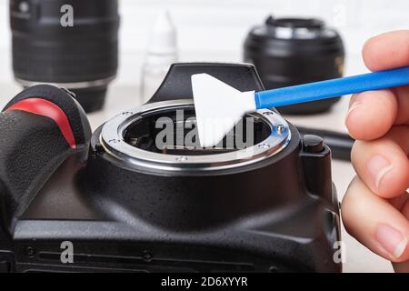 Hand, die einen feuchten Tupfer über das Kamera-Bajonett hält und das Objektiv entfernt. Routinemäßige Reinigung von Staub und Flecken von fotografischen Geräten. Nahaufnahme der Wartung. Stockfoto