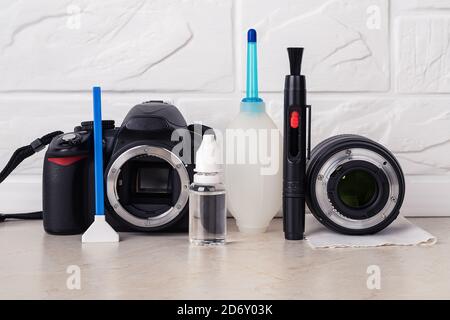 DSLR-Kamera mit offenem Bajonett, Tupfer, Flüssigkeitssensor-Reiniger, Luftgebläse, Linsenstift und Linse auf einem Mikrofasertuch über einem Tisch. Reinigungsset der Kamera. Stockfoto