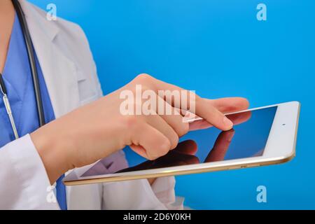 Die Krankenschwester tippt mit dem Finger auf das Tablet-Display, Nahaufnahme. Der Arzt verwendet einen Computer für die Patientenversorgung, blauer Hintergrund. Konzept der Online-Hilfe. Stockfoto