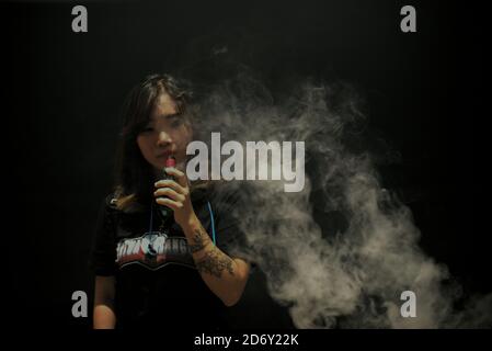 Portrait der Woman Vape Cloud Performerin Deborah Chen, nachdem sie an einem Vape Cloud Trick Contest teilgenommen hat, der während des jährlichen Vape Fest in Jakarta, Indonesien, stattfand. Deborahs Erfahrung mit dem Verdampfen begann mit einer Behandlung von Lungenentzündung und einem grünen Licht von ihrem Arzt. "Ich hatte eine Lungenentzündung in der Geschichte, benutzte Shisha-Technik als Teil meiner Behandlung. Ich fragte meinen Arzt, ob ich zu einer E-Zigarette wechseln könnte. Er sagte, es sei in Ordnung“, sagt sie. Stockfoto