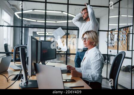 Mann wirft Papiere in die Luft. Zwei Börsenmakler in formeller Kleidung arbeiten im Büro mit dem Finanzmarkt Stockfoto