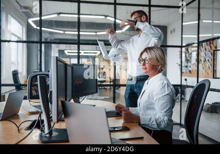 Mann wirft Papiere in die Luft. Zwei Börsenmakler in formeller Kleidung arbeiten im Büro mit dem Finanzmarkt Stockfoto