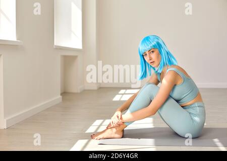 Junges Mädchen mit gefärbten Haaren sitzt auf Gummi-Matte nach Yoga-Training im modernen Fitnessstudio Stockfoto