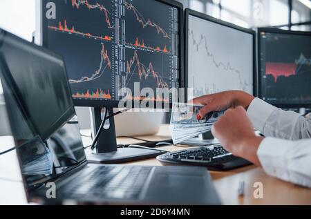 Nahaufnahme der Hände der Frau, die Geld in der Nähe hält Die Monitore mit Diagrammen Stockfoto