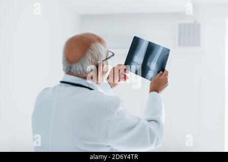 Senior-Mann Arzt in weißer Uniform untersucht Röntgen des Menschen Beine Stockfoto