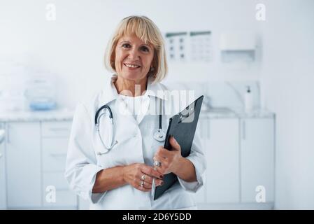 Mit Notizblock in den Händen. Porträt des Oberarztes in weißer Uniform, die in der Klinik steht Stockfoto