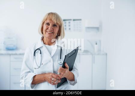 Mit Notizblock in den Händen. Porträt des Oberarztes in weißer Uniform, die in der Klinik steht Stockfoto