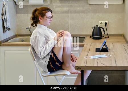 Eine Frau arbeitet sitzen in der Küche mit einem Tablette während der Isolierung durch Coronavirus-Krankheit Stockfoto