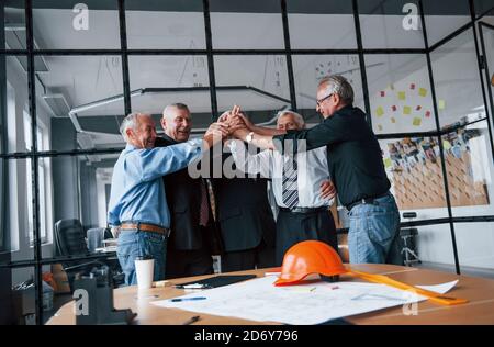 Gut gemacht, gibt sich hohe fünf. Im Büro steht ein gealtertes Team älterer Unternehmer-Architekten zusammen Stockfoto