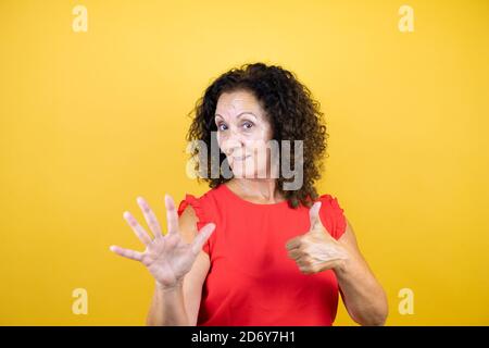 Frau mittleren Alters trägt Casual Shirt über isoliert gelb stehen Hintergrund zeigt und zeigt nach oben mit den Fingern Nummer sechs während Selbstbewusst lächeln Stockfoto