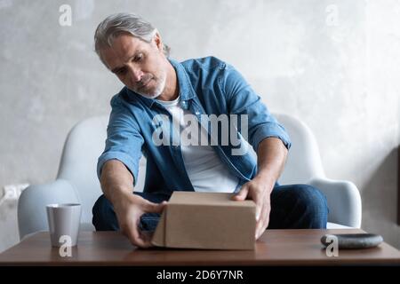 Lächelnder Mann Verbraucher offenen Karton erhalten Postpaket, männliche Kunde erhalten Kartonpaket sitzen auf Sofa zu Hause Stockfoto